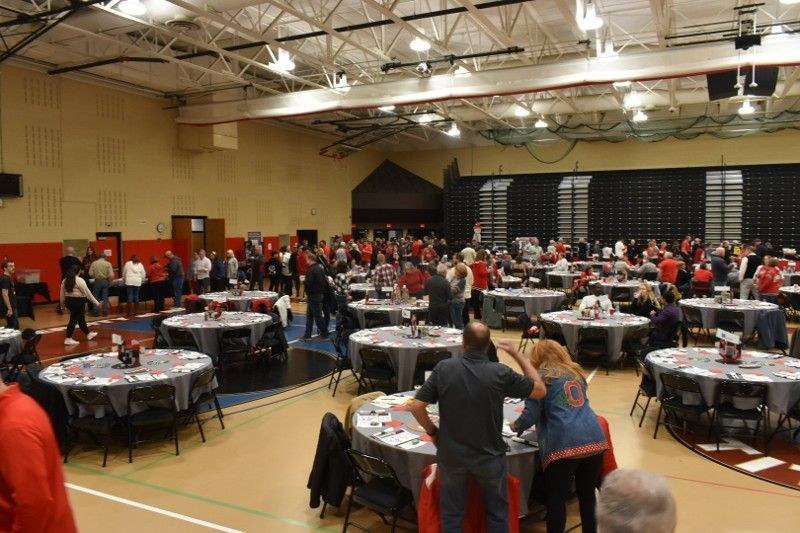 A large group of people are sitting at tables in a gym.