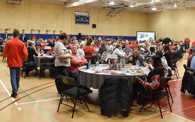 A large group of people are sitting at tables in a gym.