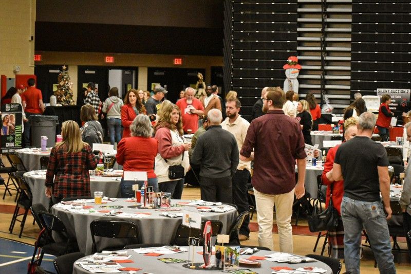 A group of people are standing around tables in a gym.