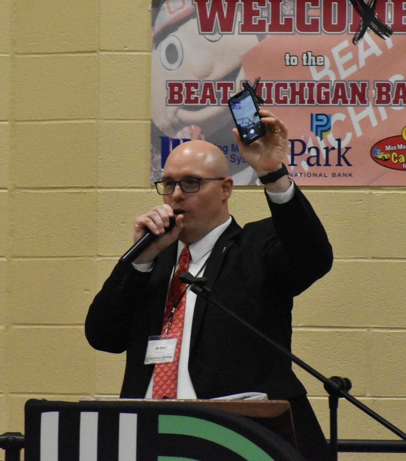 A man speaking into a microphone in front of a sign that says welcome to the beach