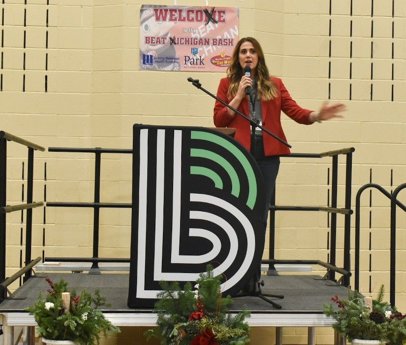 A woman is standing on a stage with a microphone in front of a sign that says welcome