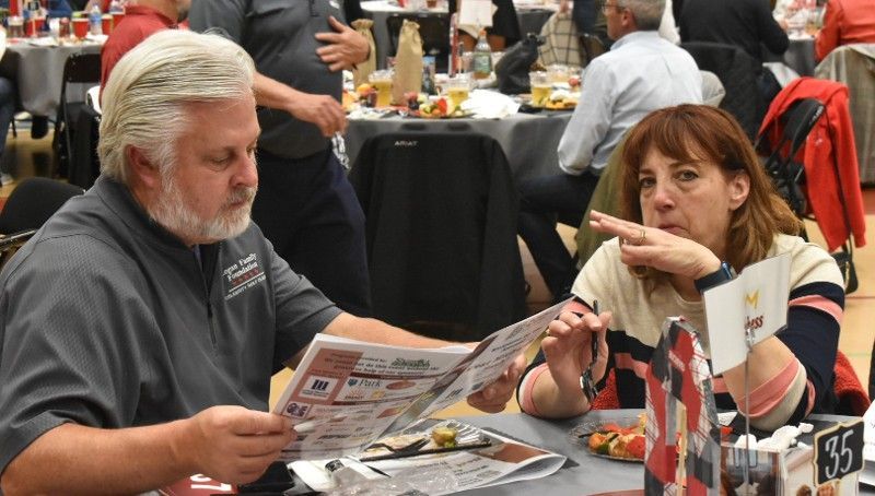 A man and a woman are sitting at a table reading a newspaper.