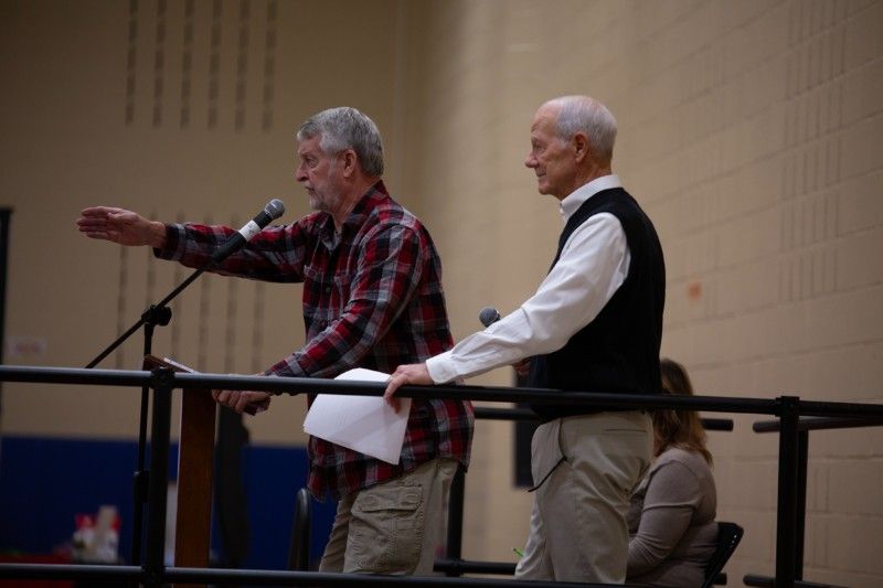 Two men are standing in front of a microphone in a gym.