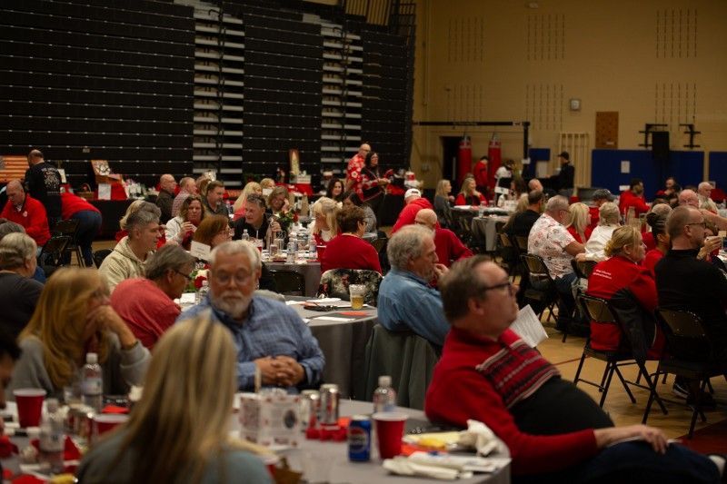 A large group of people are sitting at tables in a gym.