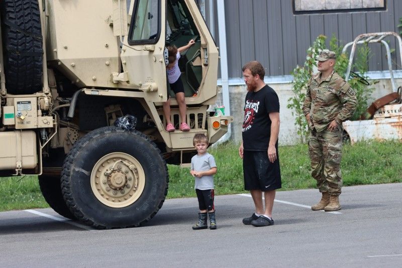 A man and two children are standing next to a military vehicle.