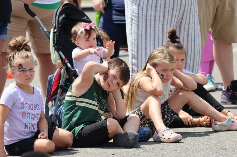 A group of children are sitting on the ground watching a parade.