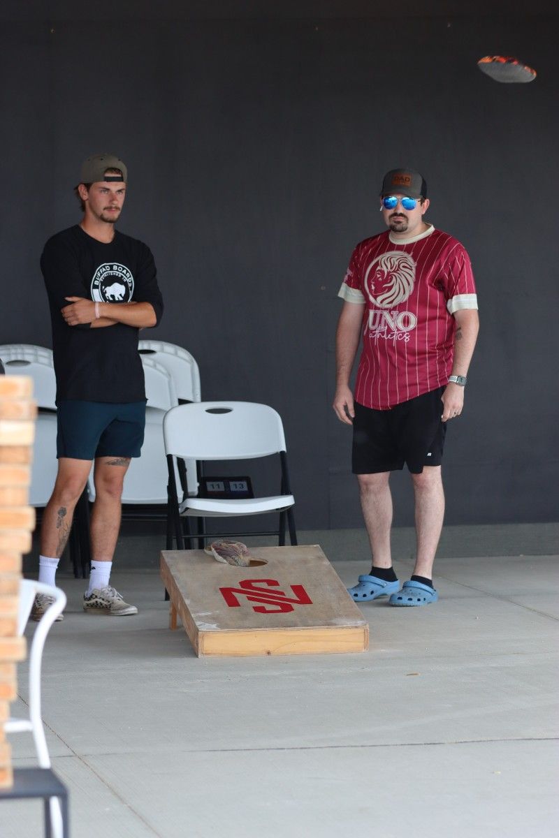 Two men are playing a game of cornhole in a parking lot.