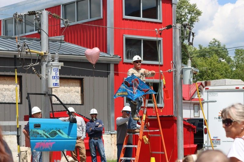 A man on a ladder holding a kite in front of a red building