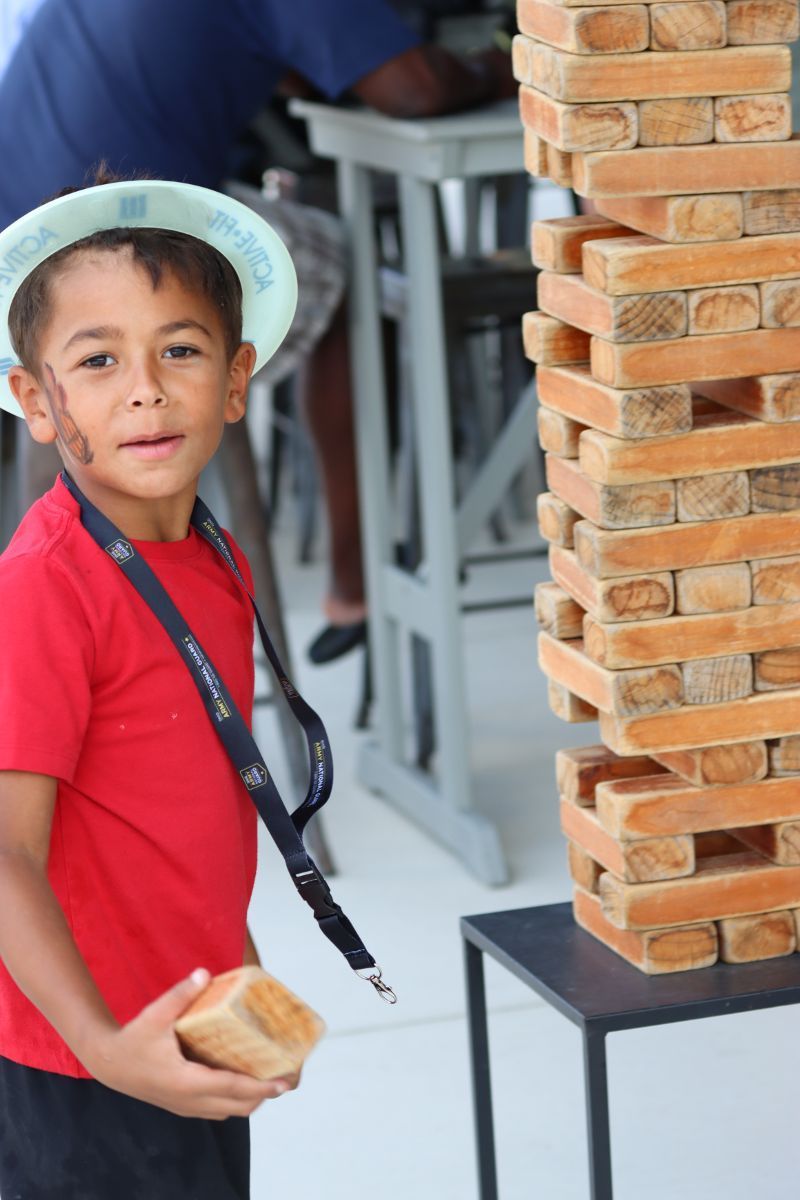 A young boy in a red shirt is standing next to a stack of wooden blocks.