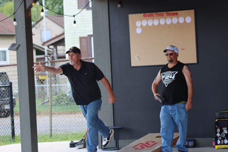 Two men are playing a game of cornhole on a porch.