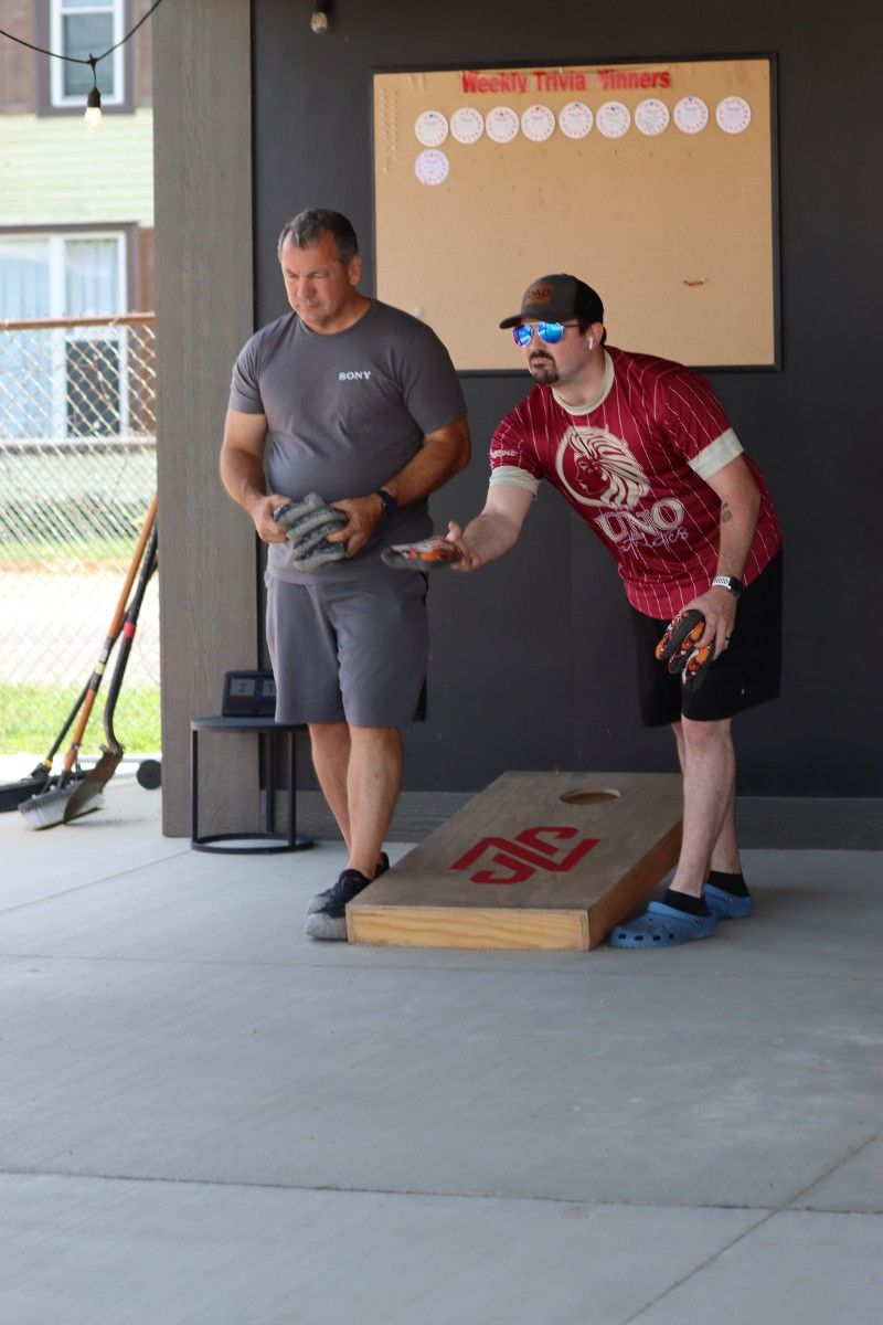 Two men are playing a game of cornhole in a garage.