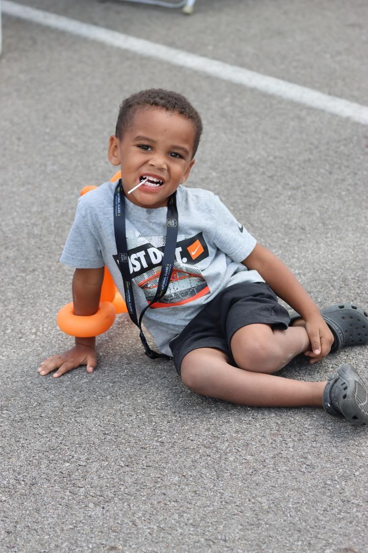 A young boy is sitting on the ground with a balloon around his neck.