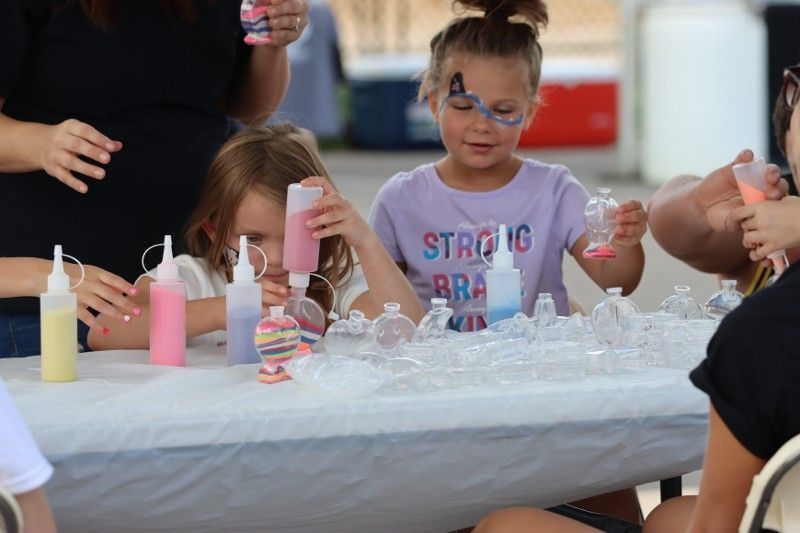 A group of young girls are sitting at a table with bottles of paint.
