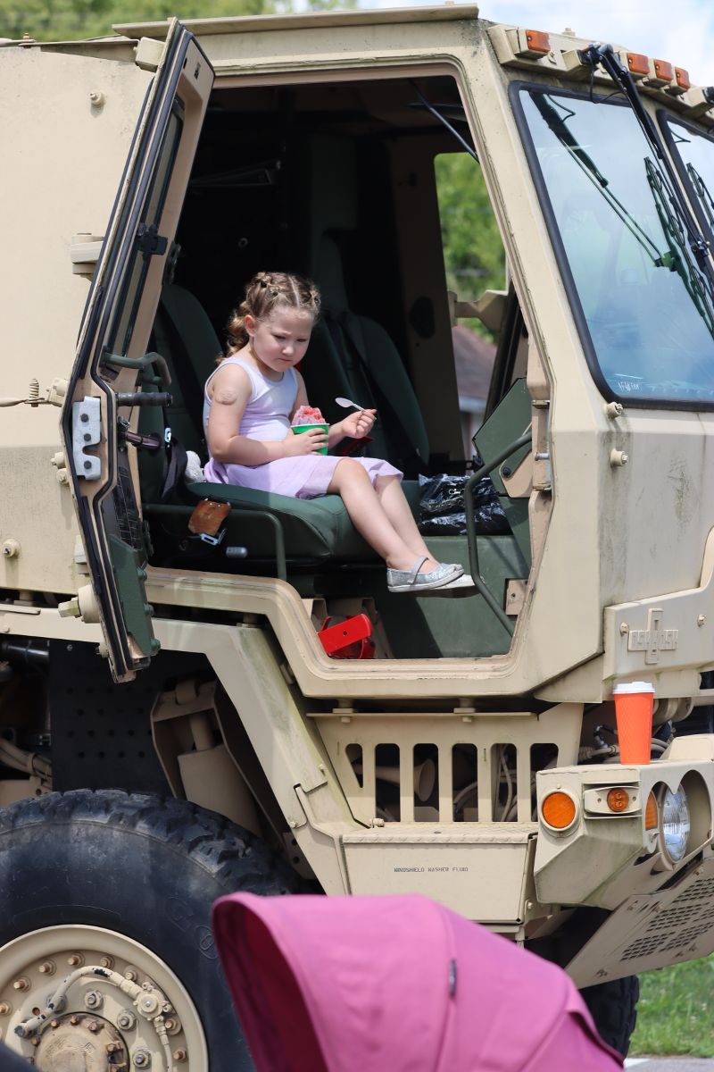 A little girl is sitting in the driver 's seat of a military vehicle.