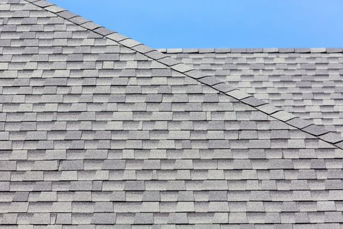 Gray shingled roof with a diagonal ridge against a blue sky