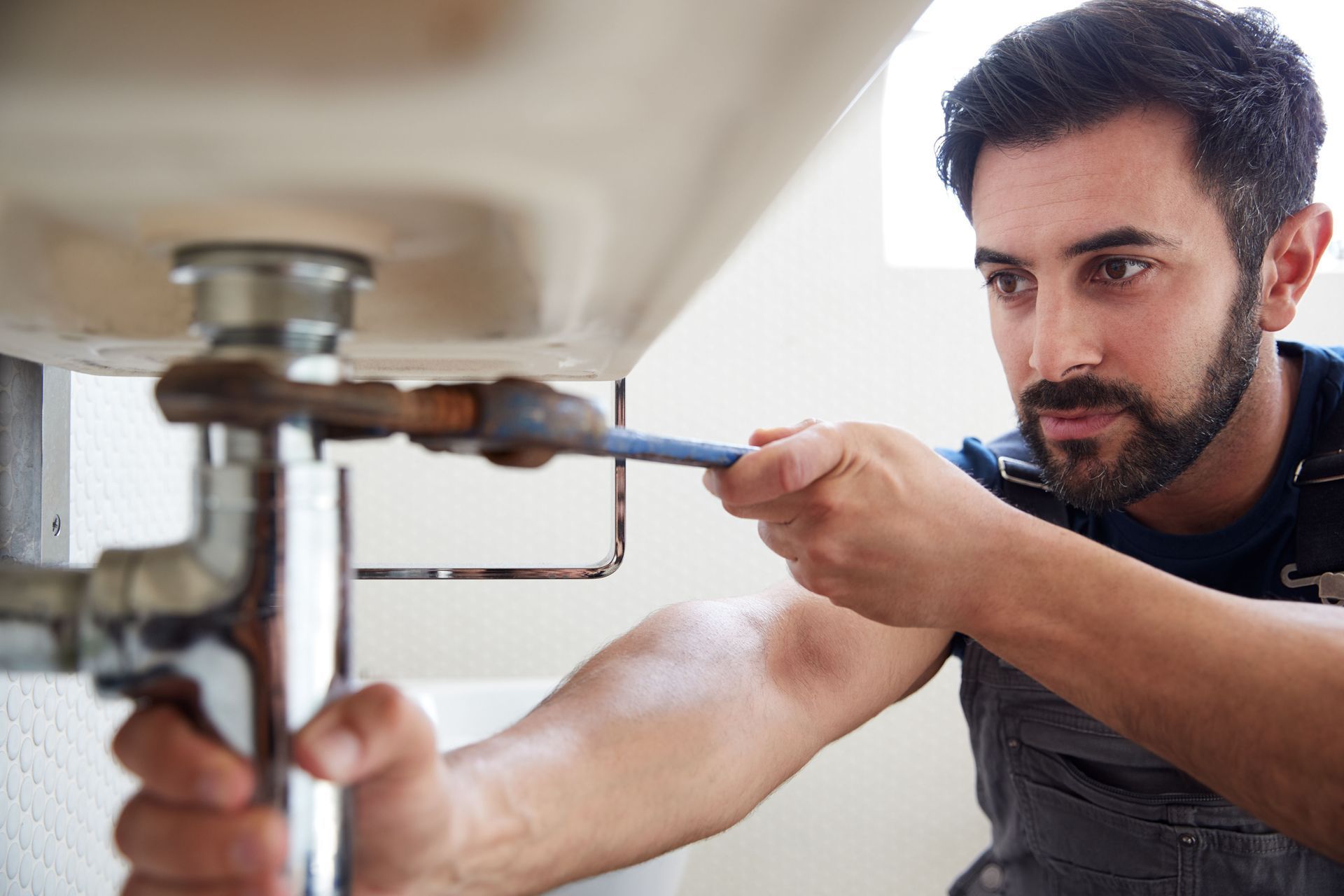 Plumber using a wrench under a white sink, working on the pipes.