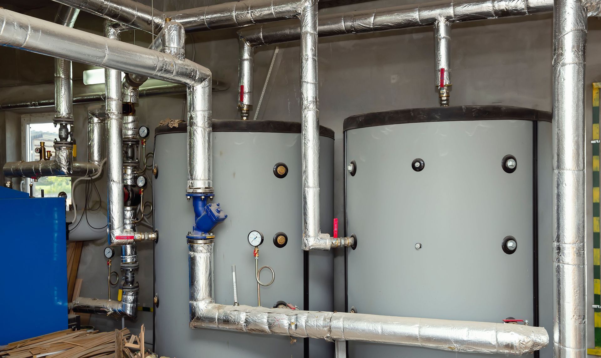 Pipes and two large gray tanks in an industrial setting. Pipes are insulated.