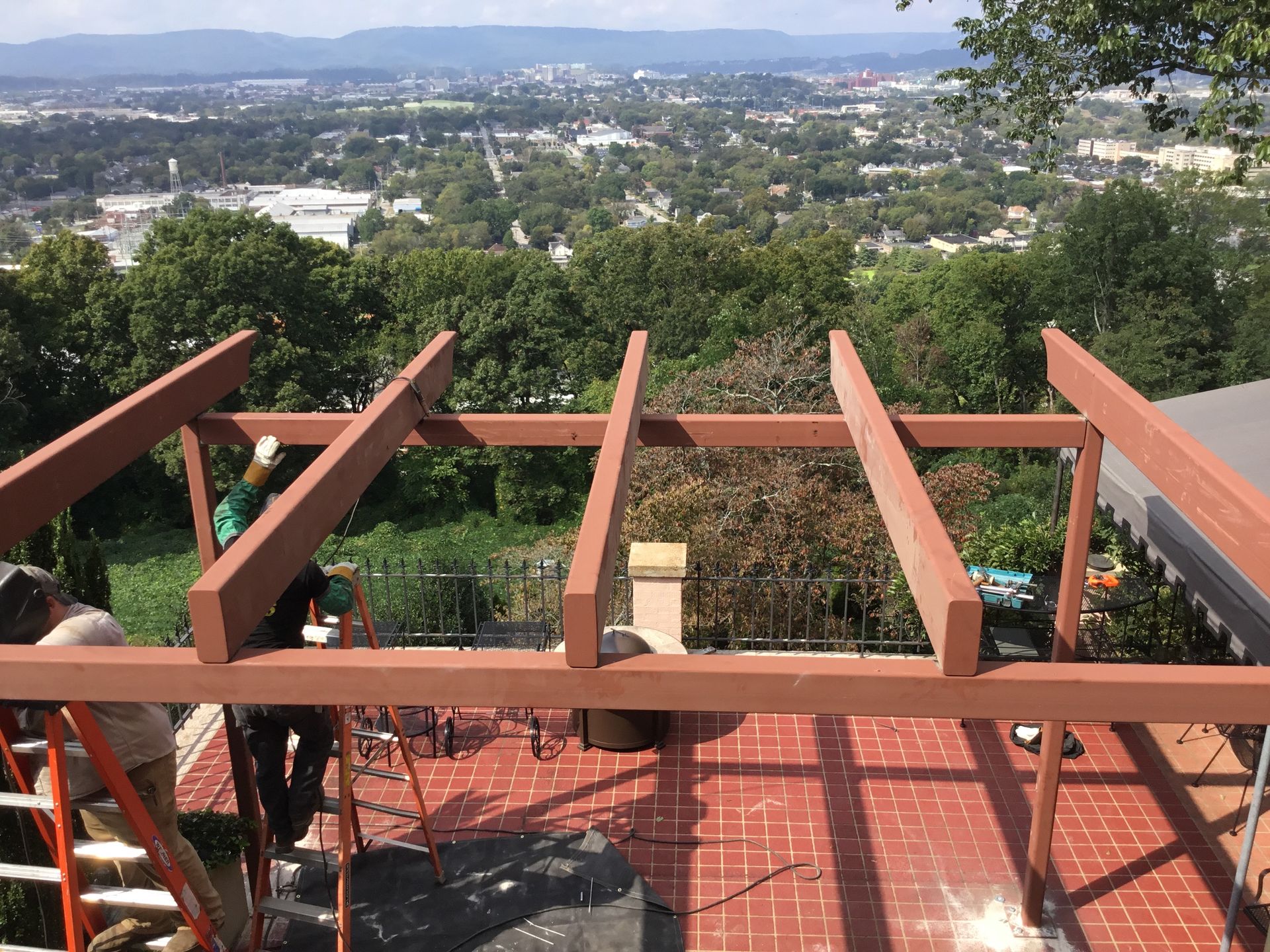 A metal structure is being built on top of a brick patio with a view of the city.