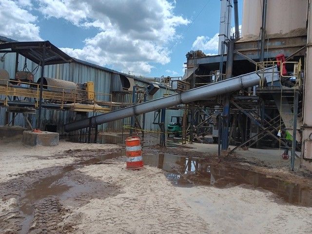 A muddy area in front of a building with a conveyor belt going through it.