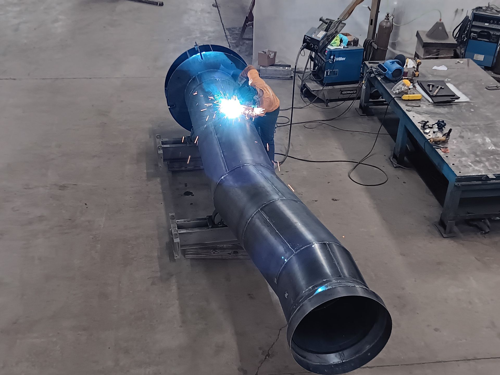 A man is welding a large pipe in a factory.