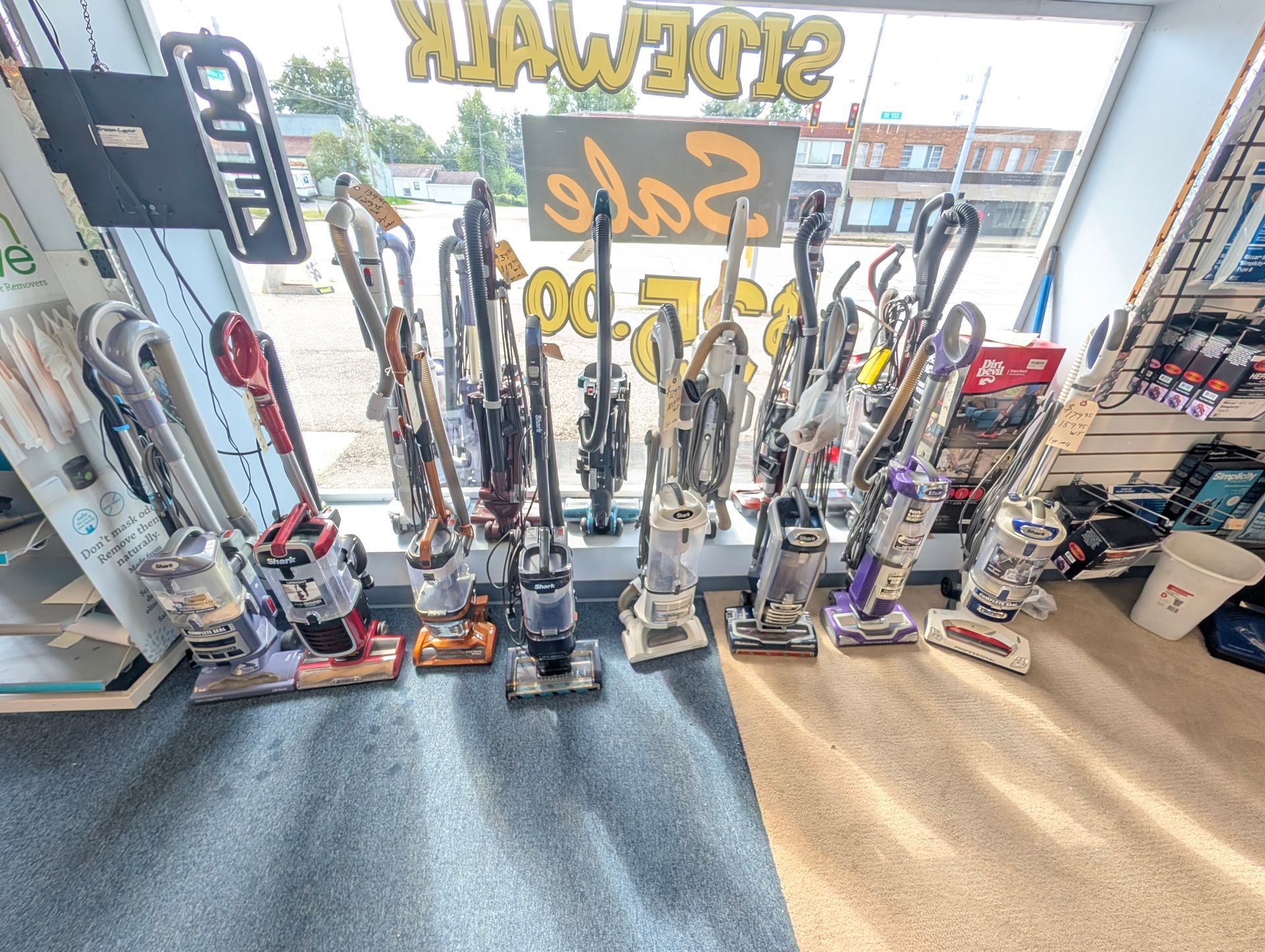 Vacuum cleaners lined up in a shop window display with mirrored glass and bright showroom lighting