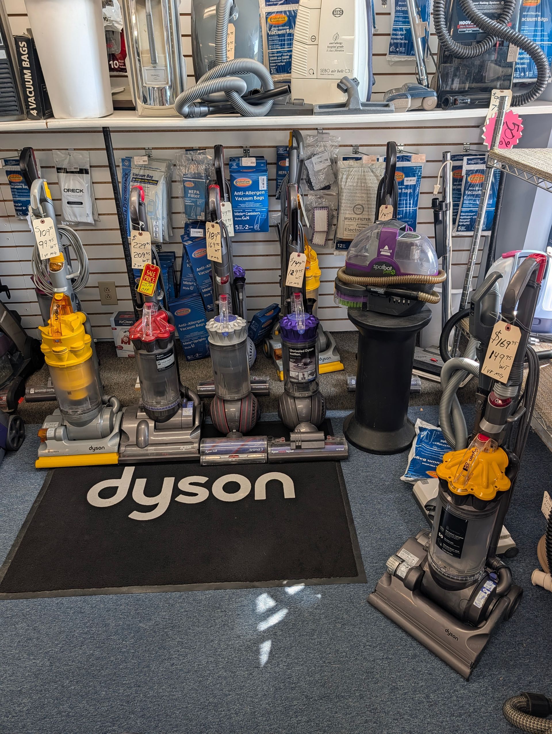 Dyson vacuum display with several upright vacuums on a showroom floor, black Dyson mat in front.