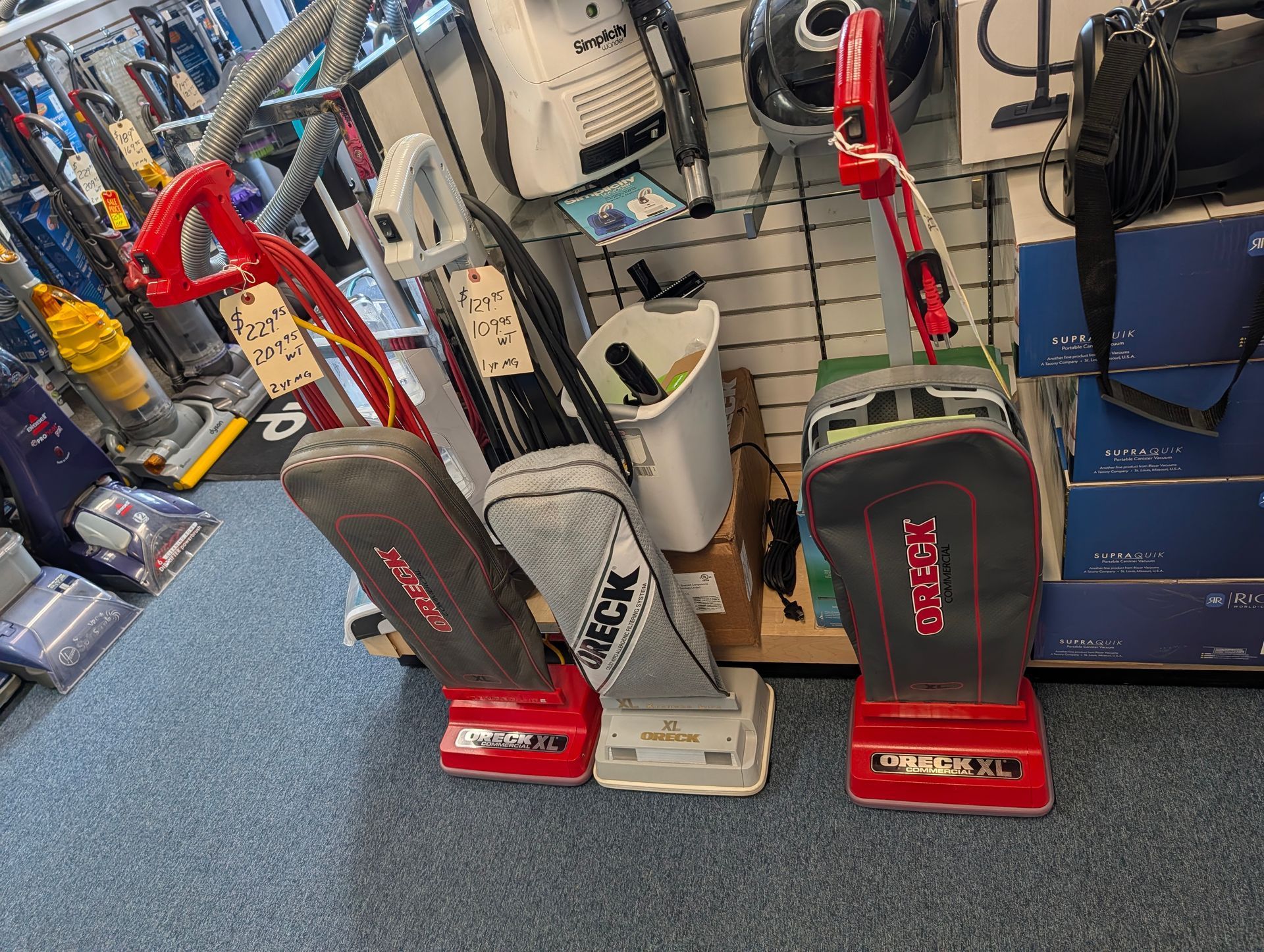 Two upright vacuum cleaners on display in a store aisle, one red and one gray