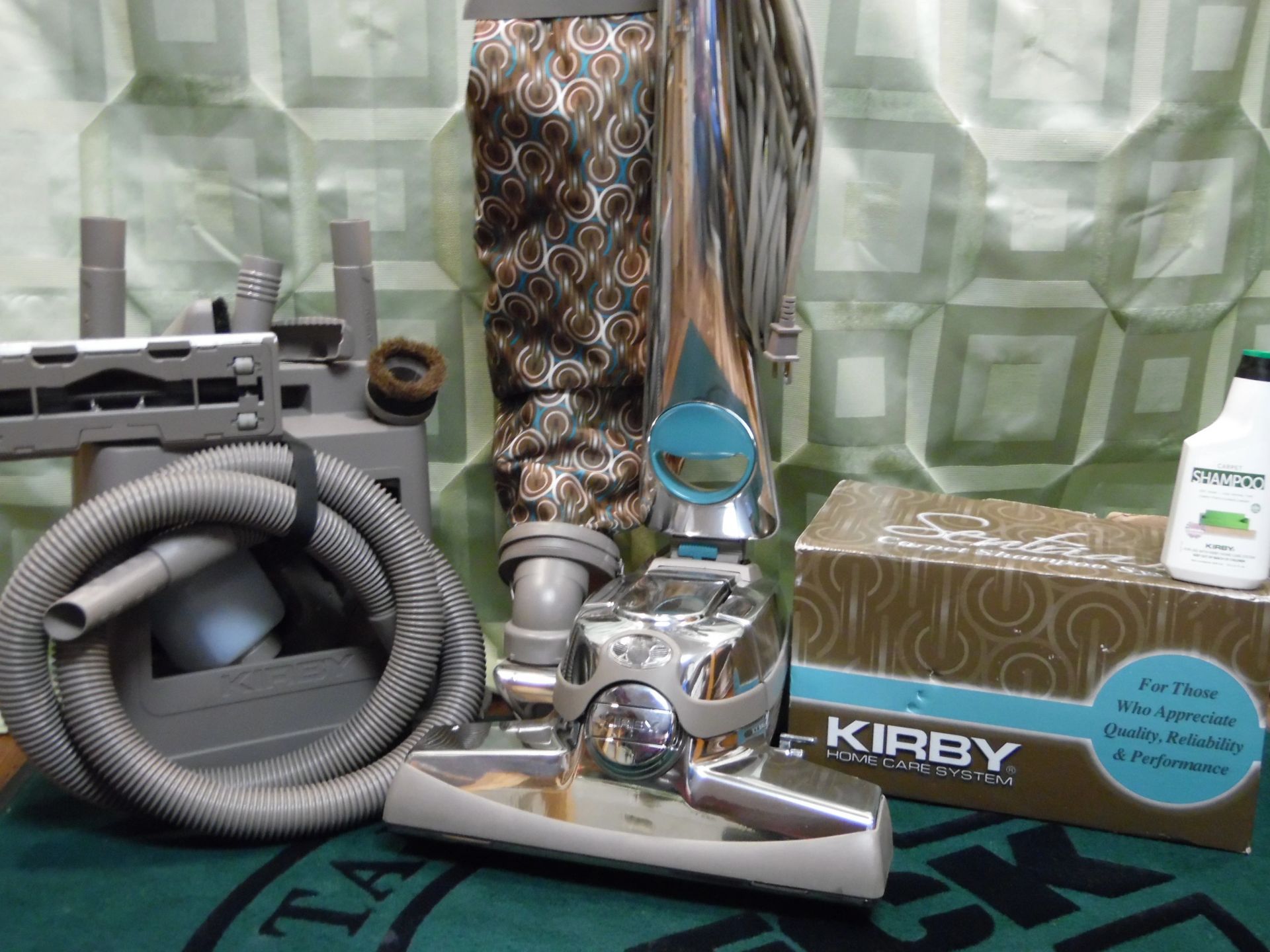Kirby vacuum cleaner with hose, attachments, and box displayed on a green patterned surface
