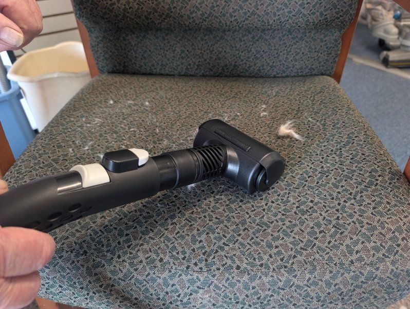 Handheld vacuum cleaner nozzle cleaning a patterned fabric chair seat