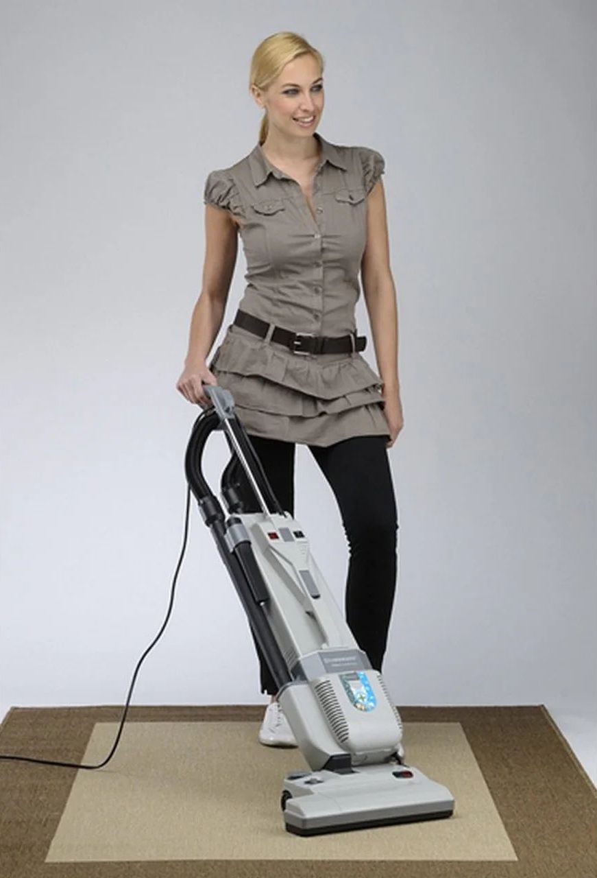 Woman using a vacuum cleaner on a carpeted floor in a room.
