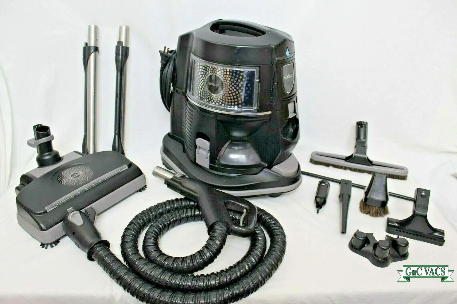 Black canister vacuum cleaner with hoses, attachments, and tools arranged on a white background