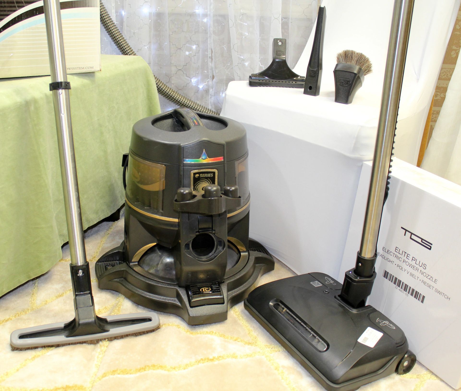 Vacuum cleaner parts and attachments are displayed on the floor, including upright and floor nozzles.