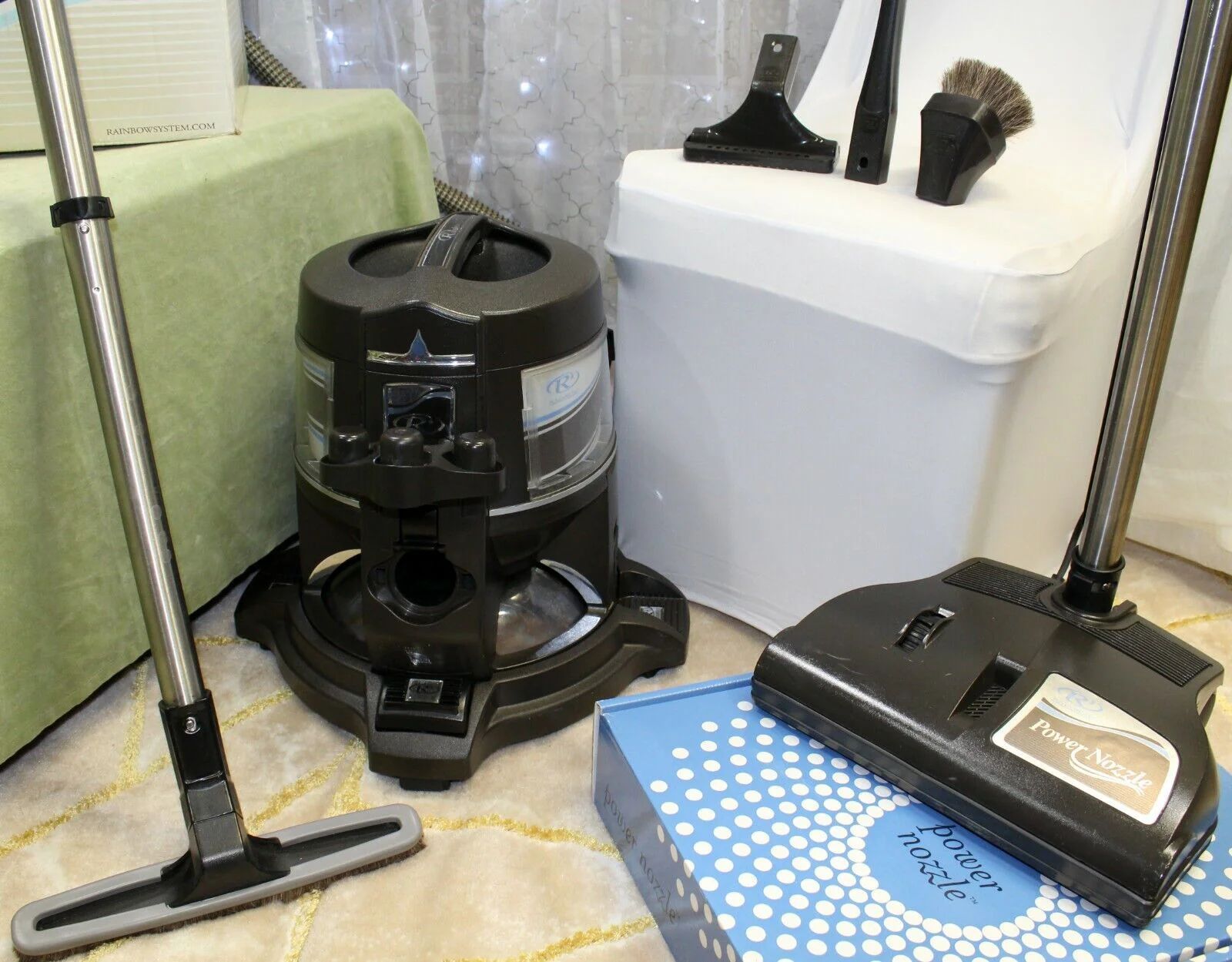 Three vacuum cleaners and a blue steam mop on a bathroom floor beside a toilet.