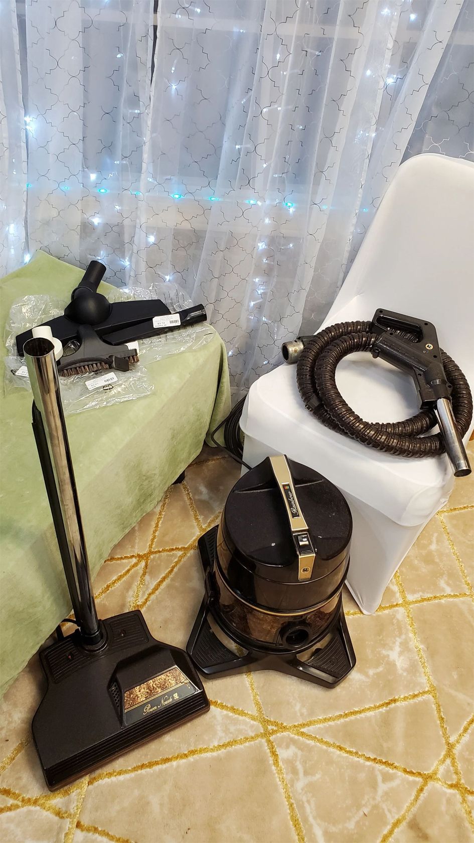 Vacuum cleaner and floor tools on a tiled floor with sheer curtains behind