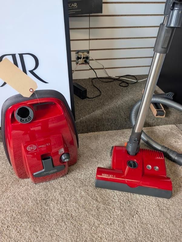 Red vacuum canister and upright vacuum head on beige carpet