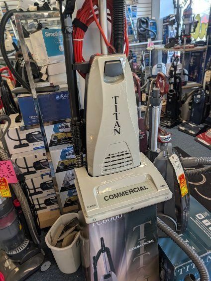 White upright commercial vacuum cleaner displayed in a store aisle with other cleaning equipment