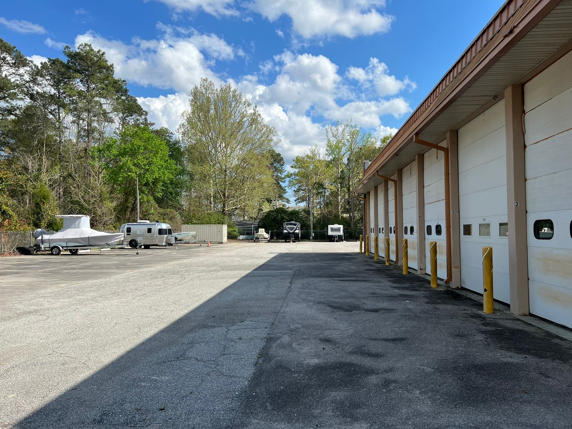 Parking lot with storage units; vehicles parked on left, blue sky.