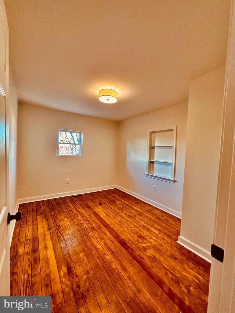 An empty bedroom with hardwood floors and a window.