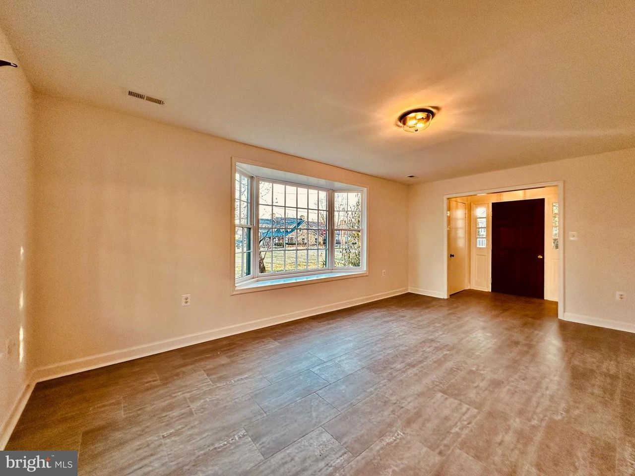 An empty living room with hardwood floors and a large window.