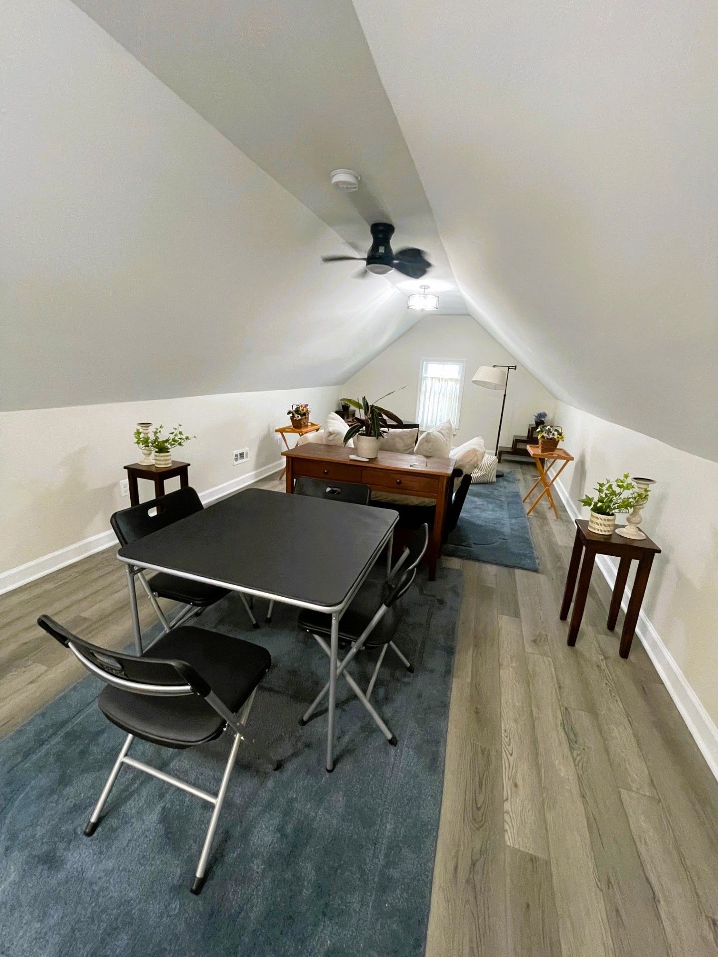 Attic room with a table and chairs in it and a ceiling fan.