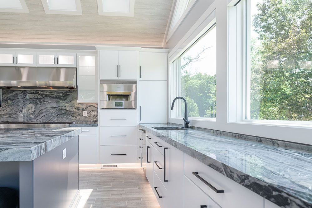 A kitchen with white cabinets, granite counter tops, stainless steel appliances and a large window