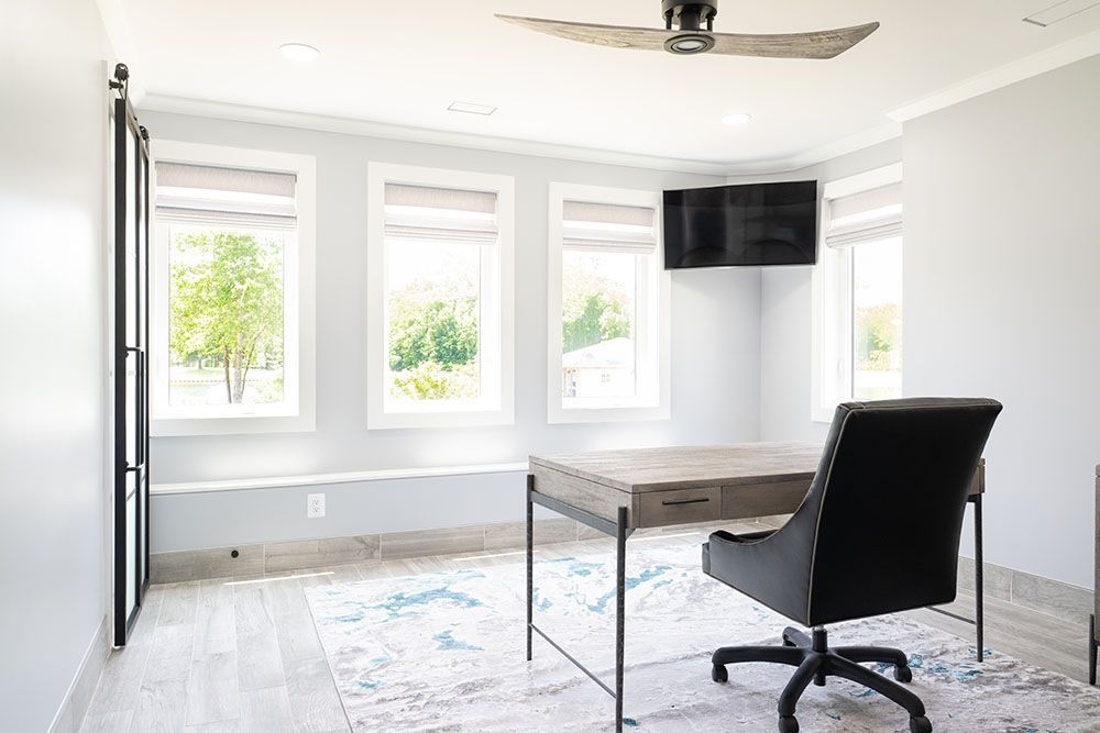 A home office with a desk, chair, television and ceiling fan