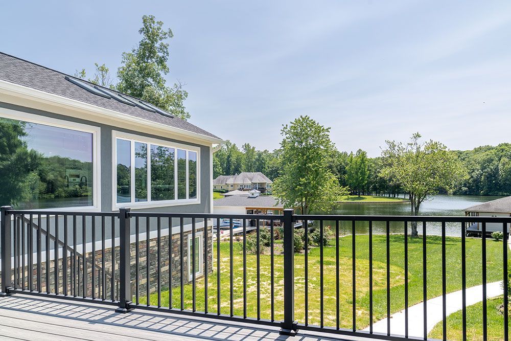 A deck with a railing overlooking a lake and a house