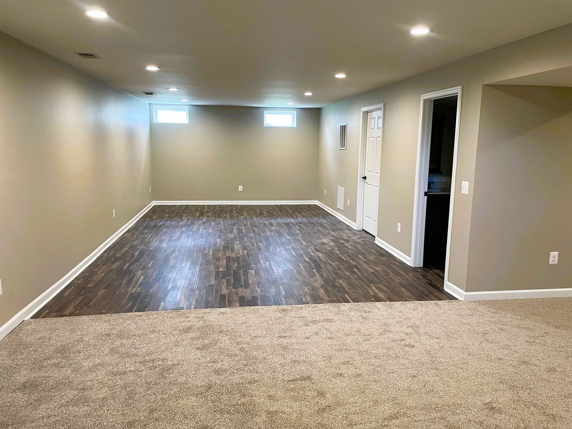 An empty basement with hardwood floors and tan walls.