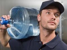 A man is carrying a large water bottle on his shoulder.