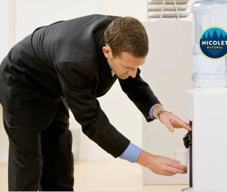 A man in a suit is pouring water into a cup from a water dispenser