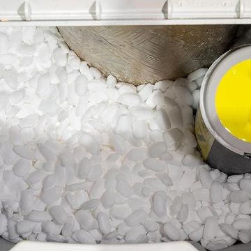 A bucket of yellow paint is sitting on top of a pile of white rocks.