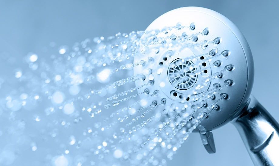 A close up of a shower head spraying water on a blue background.