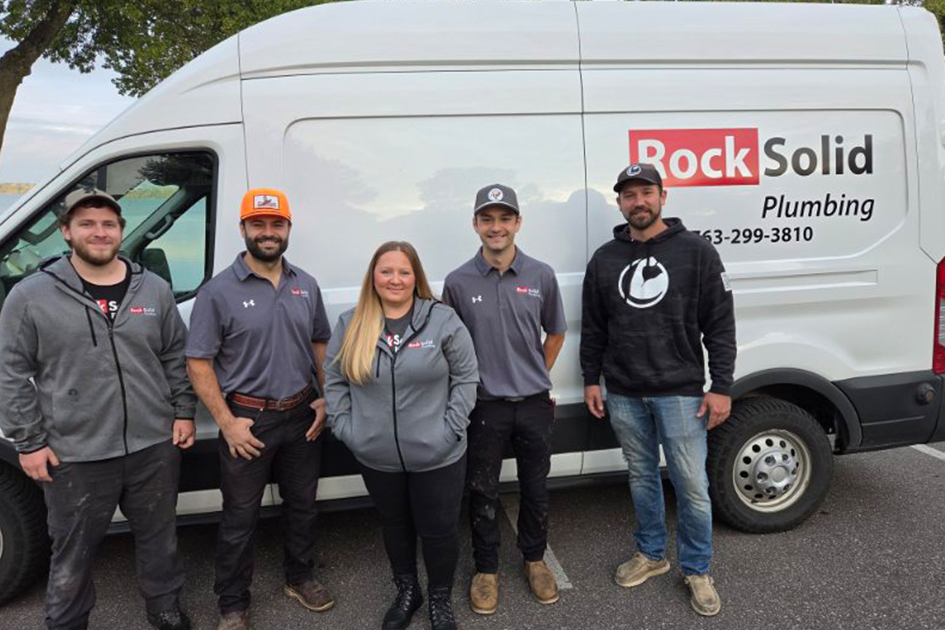 Five Rock Solid Plumbing employees standing in front of a white service van