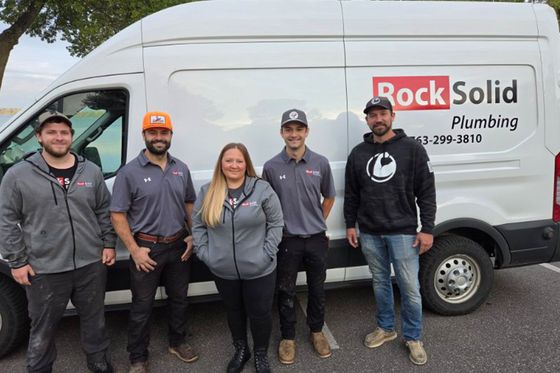 Five plumbers standing in front of a Rock Solid Plumbing service van